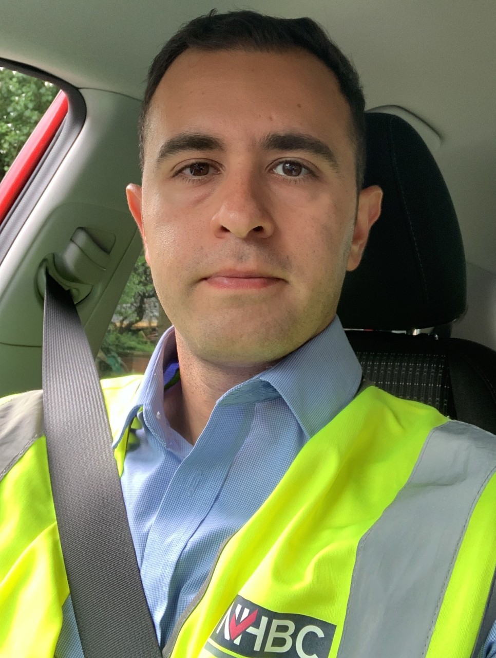 a man, sat in a car in site safety clothing looking at the camera