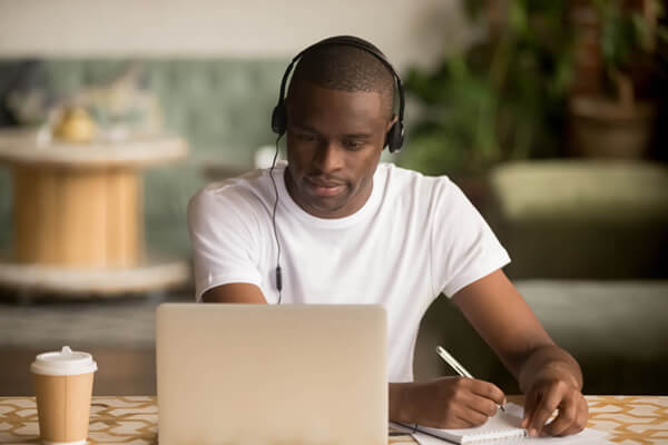 a photo of a man sitting at a laptop wearing headphones