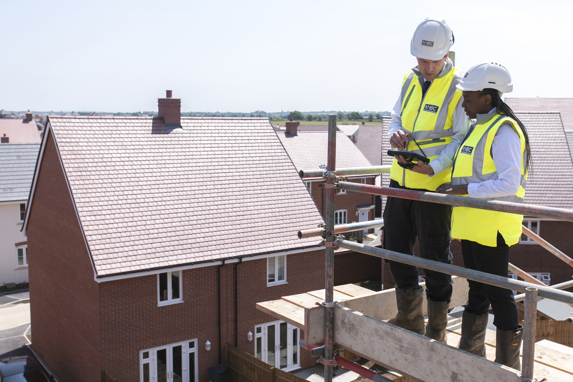 a photo of two people in site safety clothing viewing a site from some scaffolding