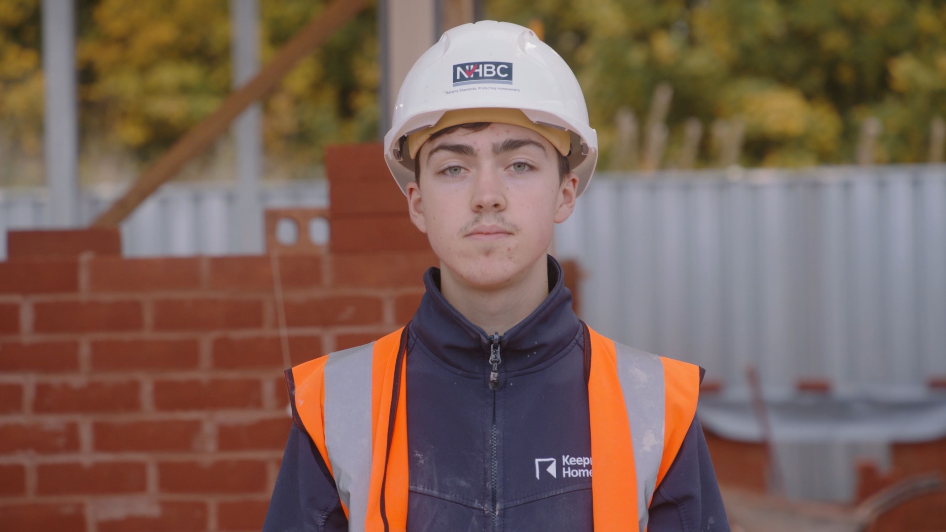 a young man in an orange high vis vest and white hard hat looking at the camera