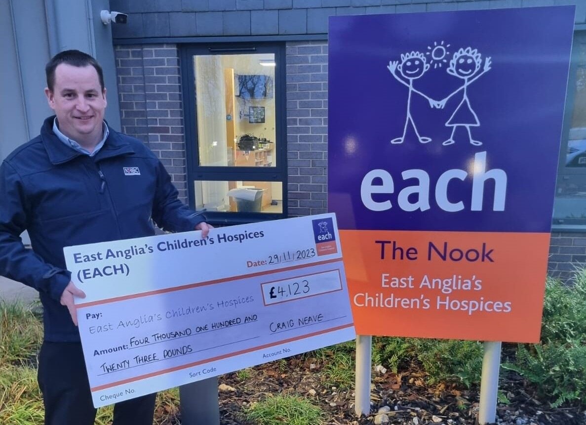 a man in a nhbc jacket holding a check for a charity outside a children's hospice
