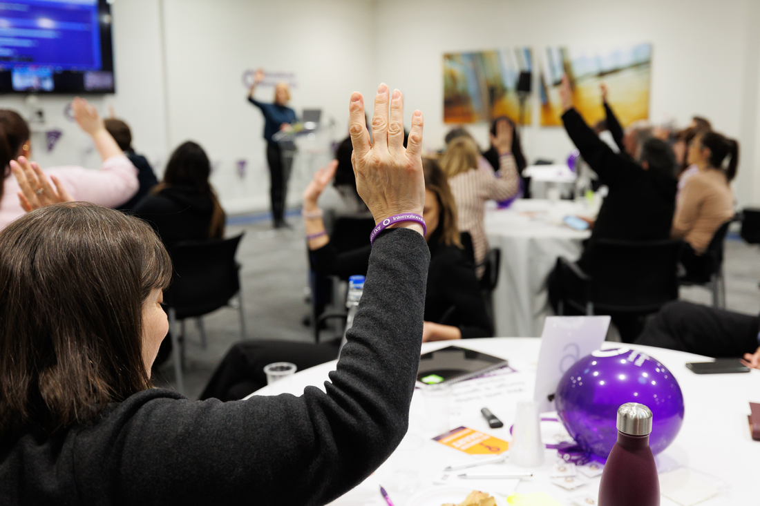 a group of women in a conference room raising their hands to show purple wristbands