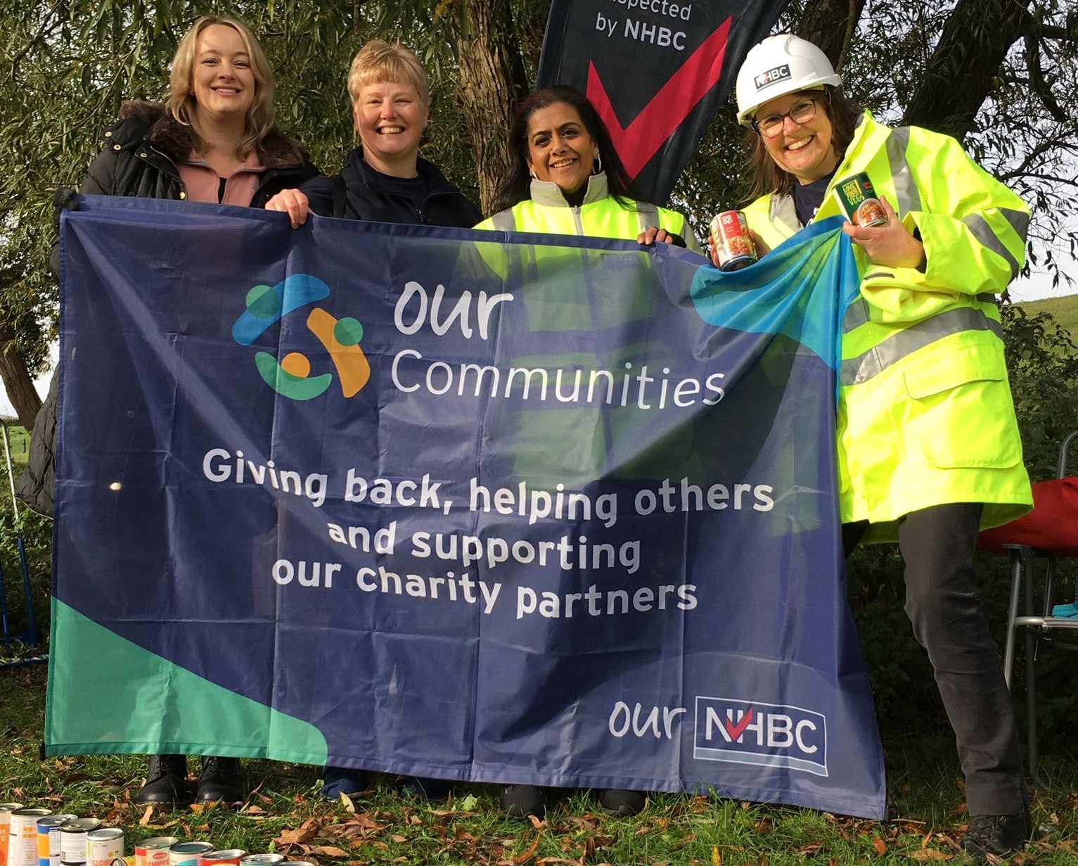 four nhbc staff members holding an 'our communities hero' flag while smiling at the camera