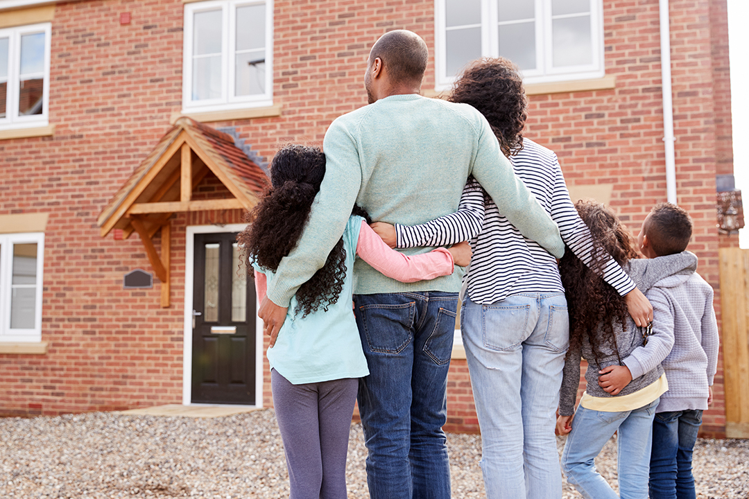 a family hugging with their backs to the camera as they look at their new home