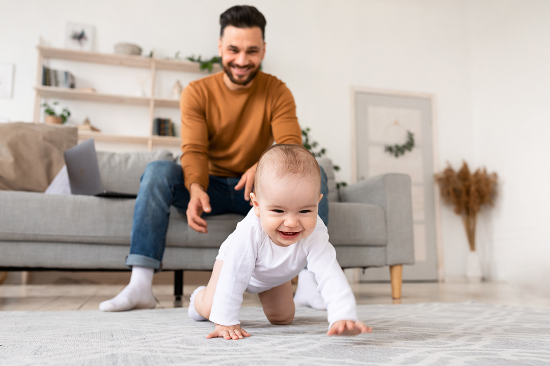 a man and his baby laughing as the baby crawls in a modern-looking living room