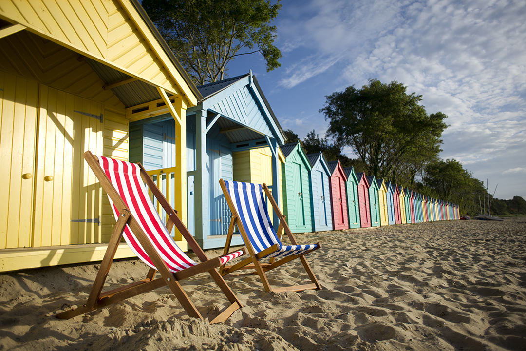 a row of colorful beach houses with striped deckchairs on the sand