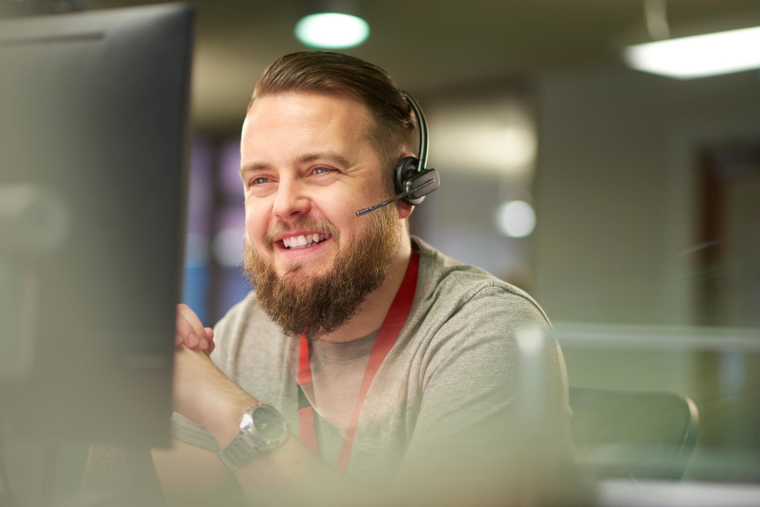 a bearded man wearing a headset in an office, smiling