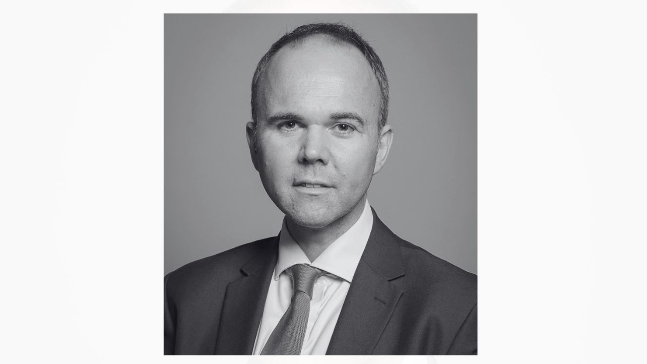 a black and white photo of gavin barwell in a suit smiling at the camera