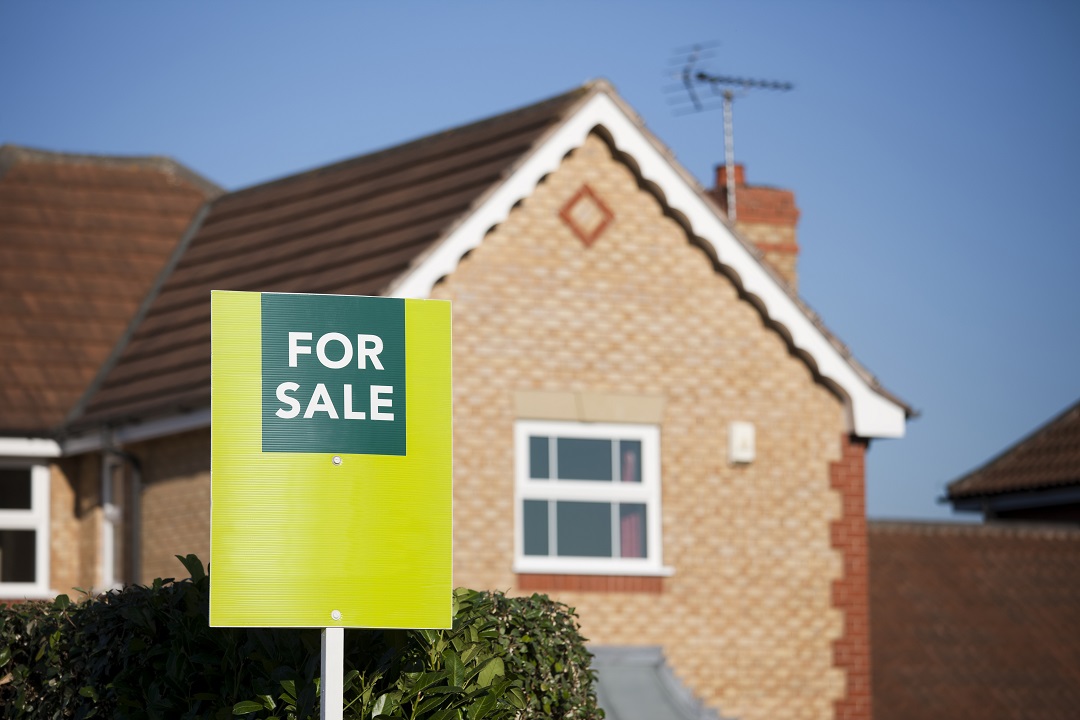 a photo of a red brick house with a for sale sign in front of it and a blue sky in the background