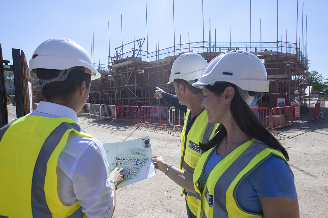 two men and a woman wearing high vis jackets and hard hats looking at building plans