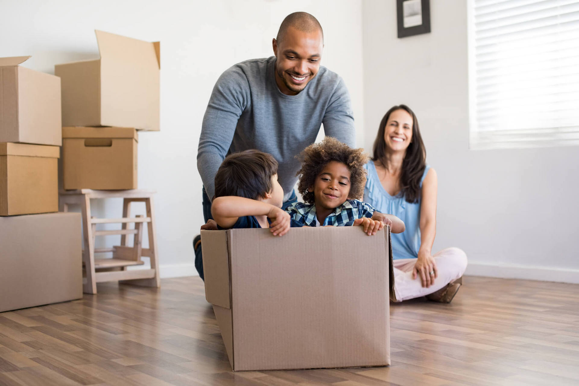 a couple laugh as their children sit inside an empty cardboard box on the floor