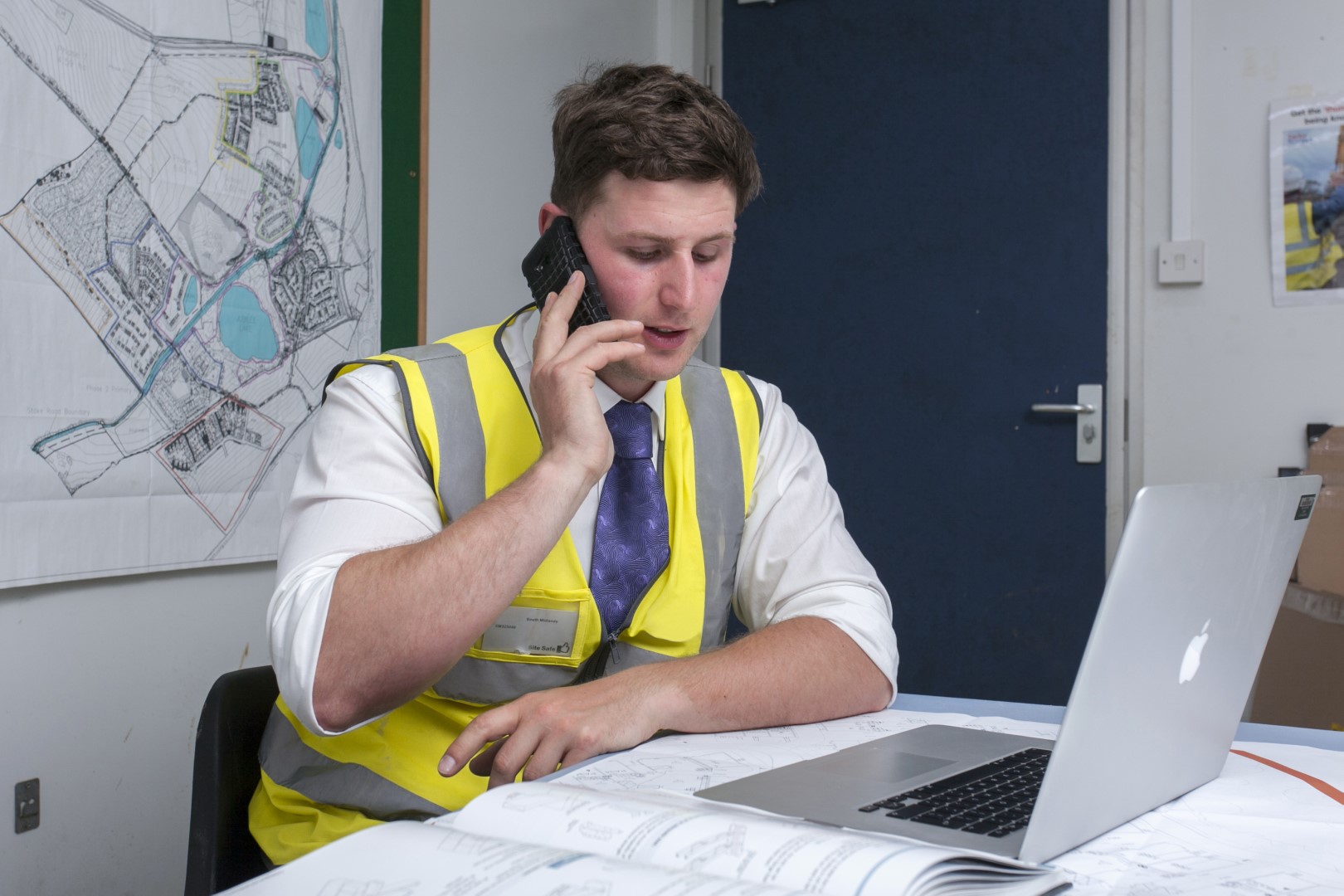 a guy wearing site safety clothing sitting in an office talking on the phone