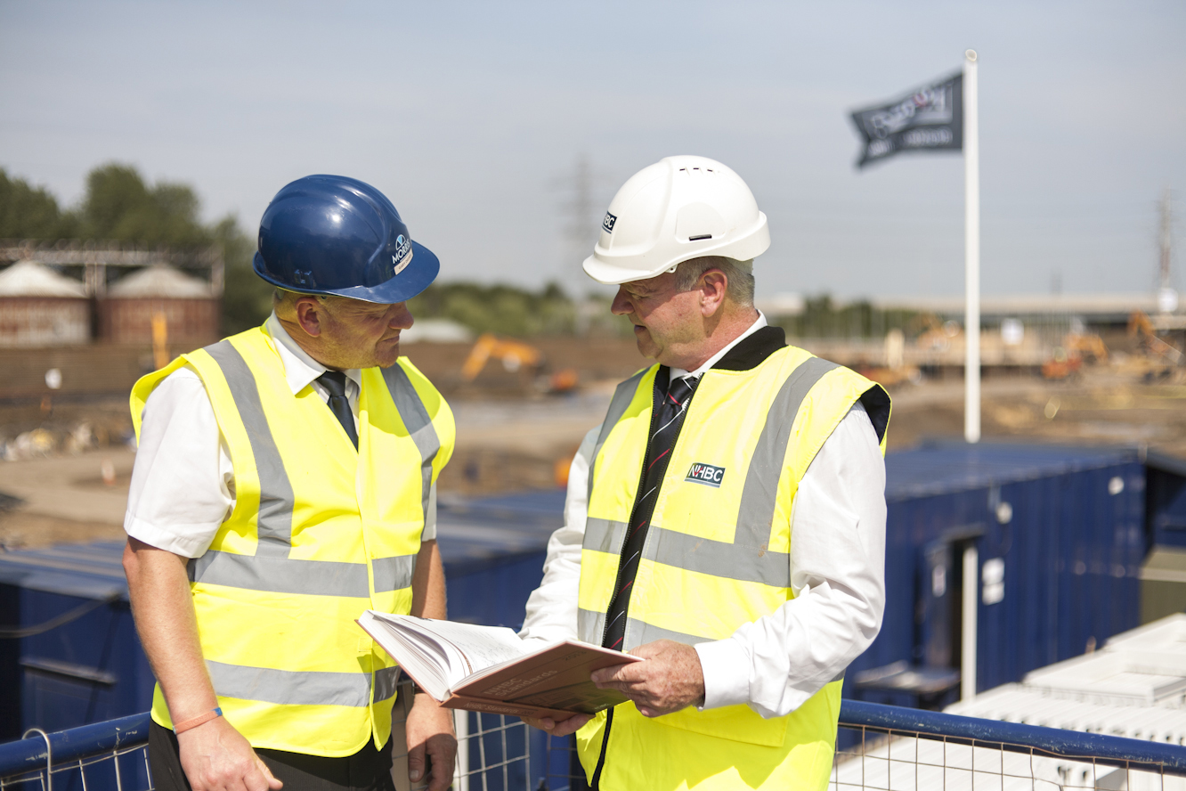 two people wearing site safety clothing and hard hats discussing an inspection