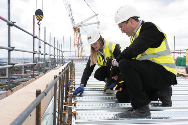 two people in site safety clothing and hard hats inspecting work done on a roof