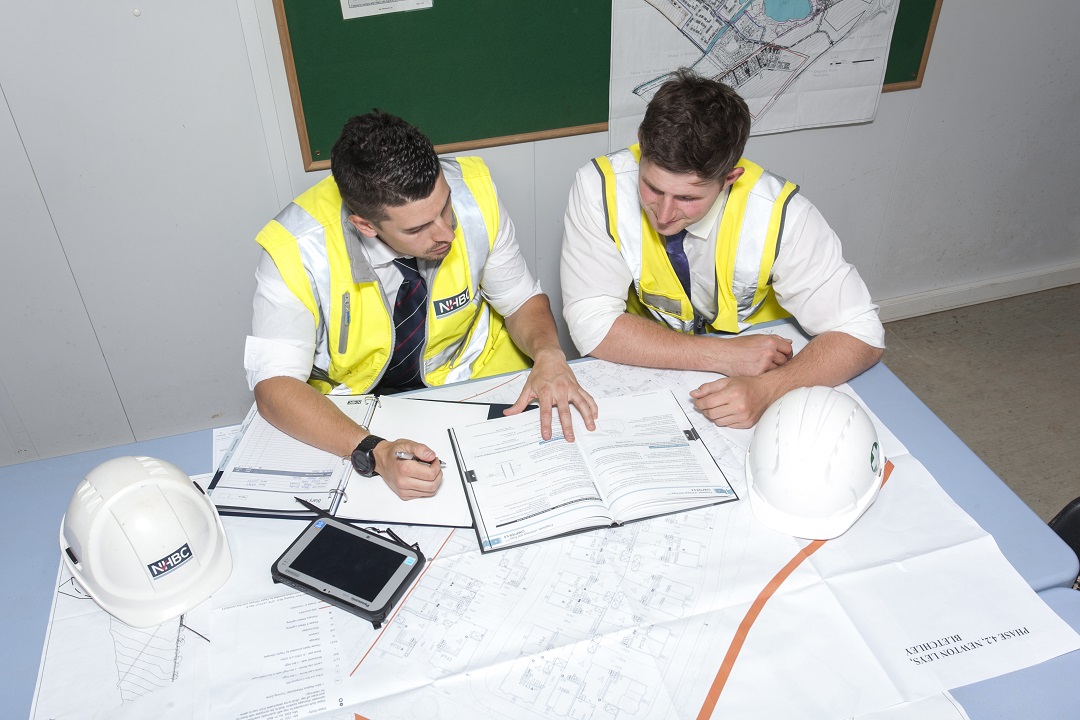 a photo of two people having a conversation at a table while wearing site safety clothing
