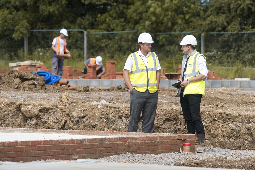 two men in site safety clothing and hard hats inspecting foundations on a site