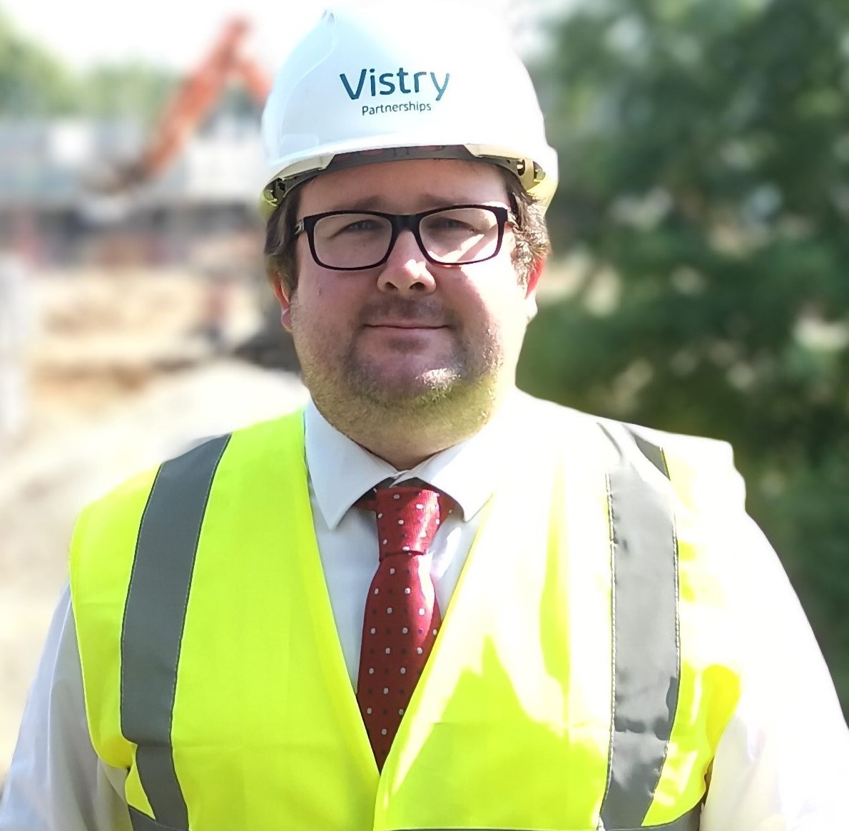 a man in a shirt and tie and site safety clothing smiling at the camera