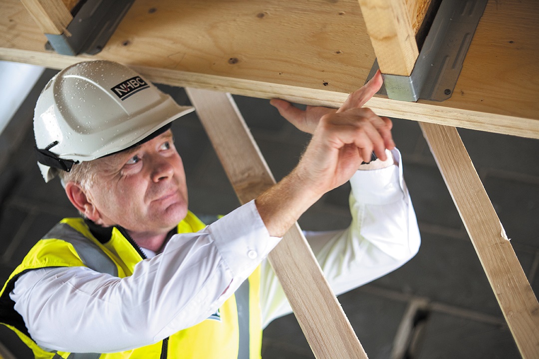 a man in site safety clothing investigating a metal joist on a wooden beam