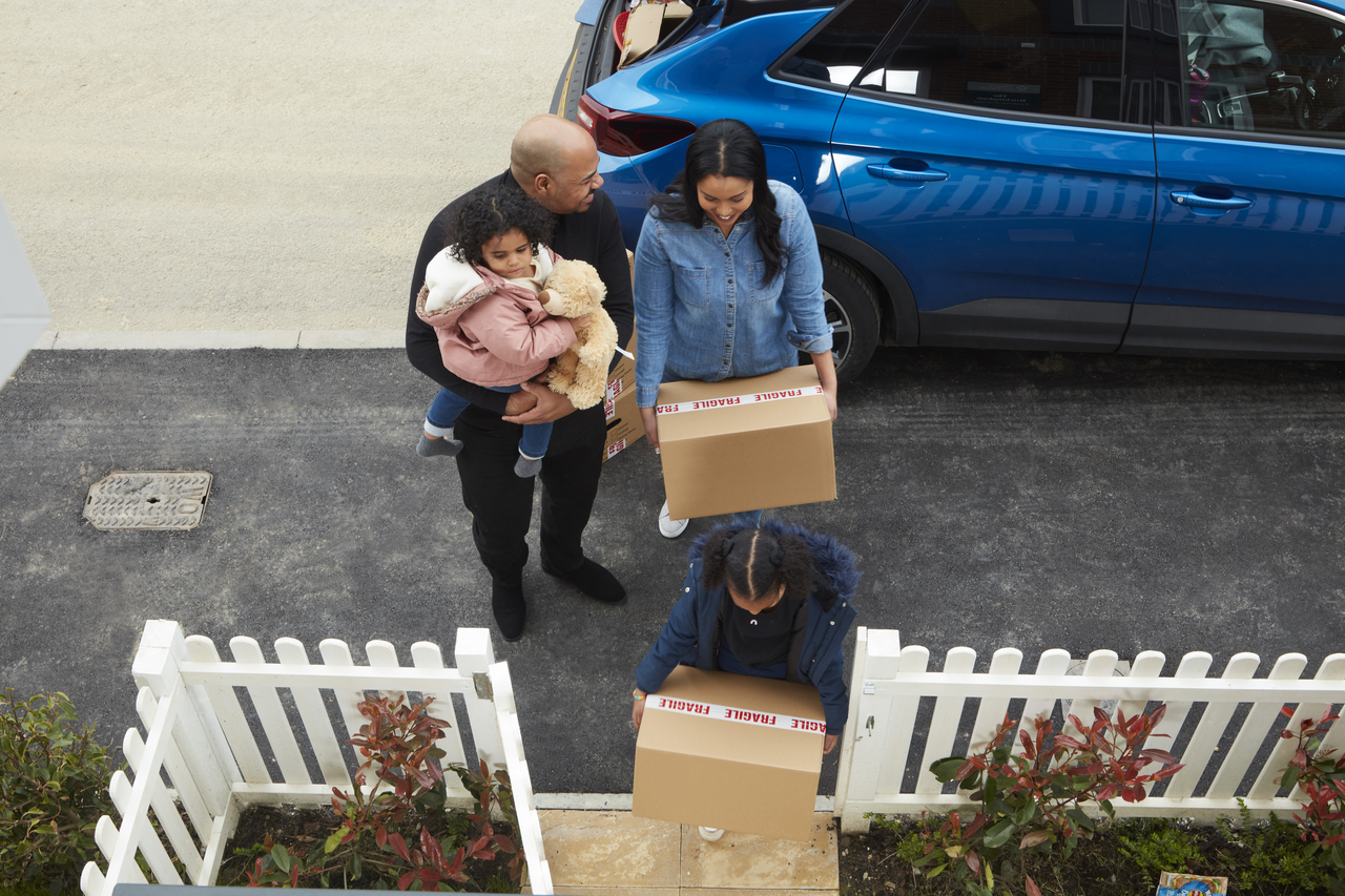 a young family moving into a new home, carrying a cardboard box