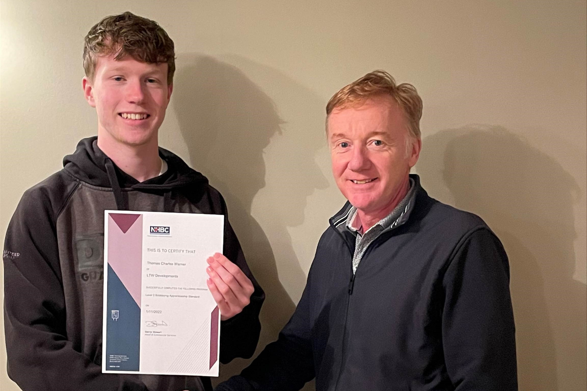 two people smiling at the camera while holding an apprenticeship certificate