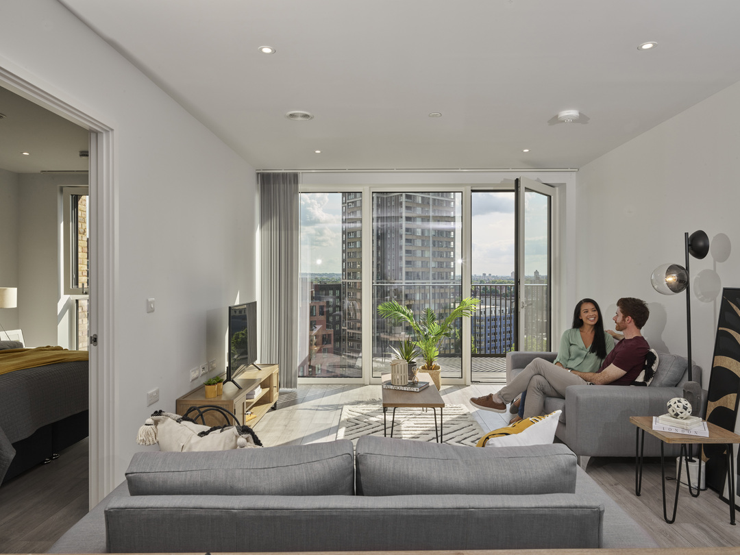 a modern looking living room with balcony views of a city with a couple sitting together on the sofa
