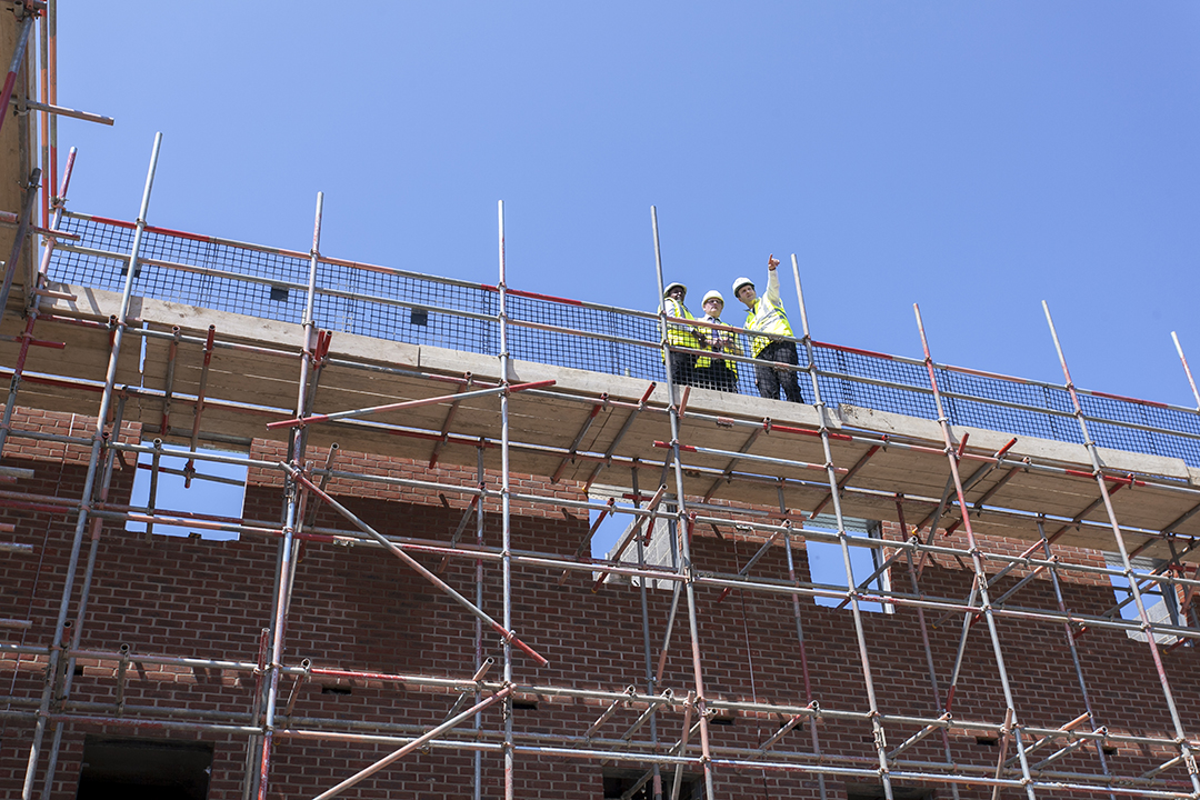 three people on scaffolding wearing site safety clothing and hard hats