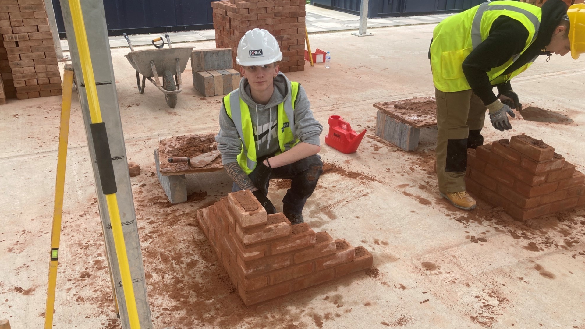 a photo of a young man in site safety clothing kneeling by some brickwork
