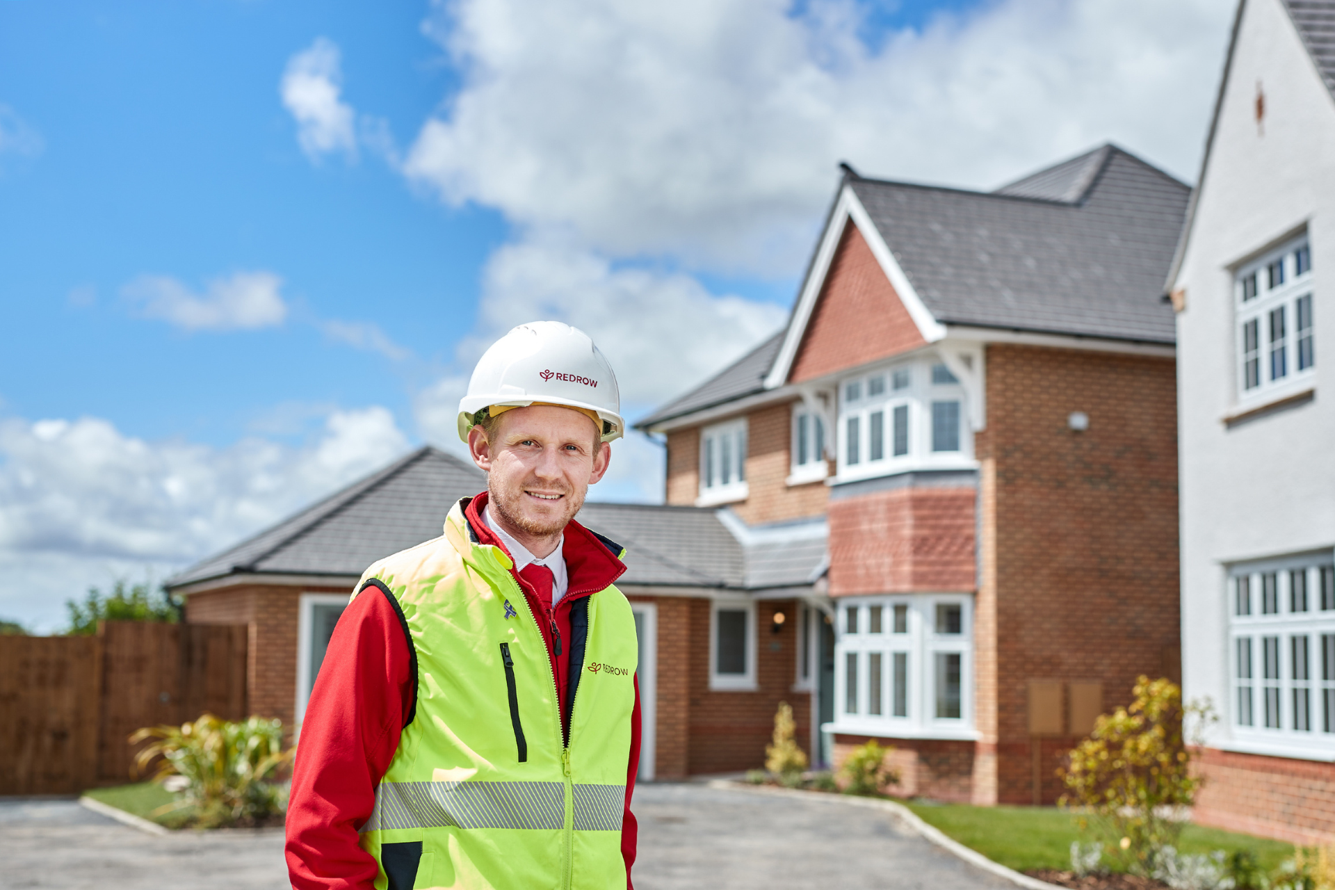 a photo of a young man in site safety clothing in front of new build houses