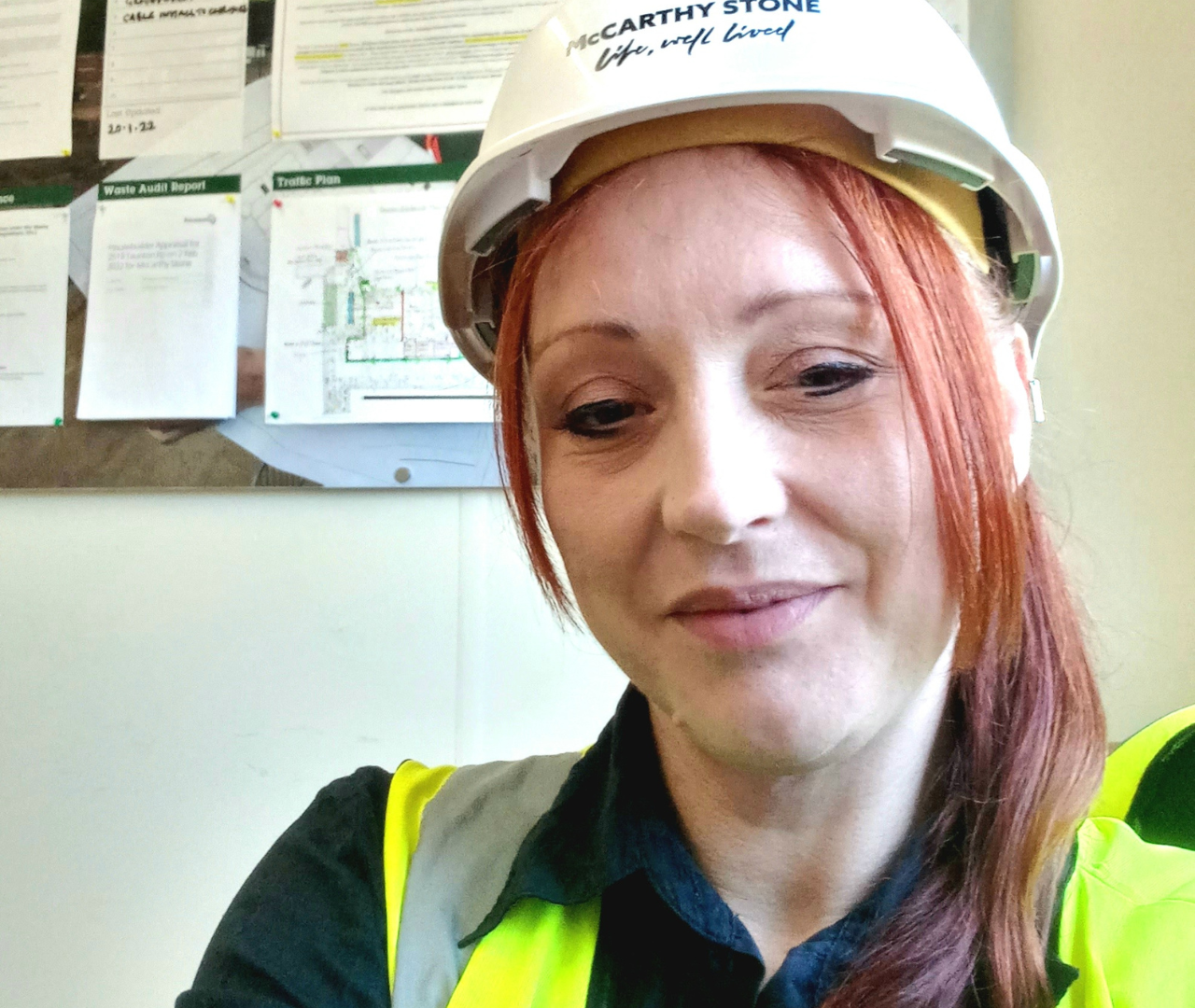 a woman in site safety clothing and a hard hat smiling at the camera