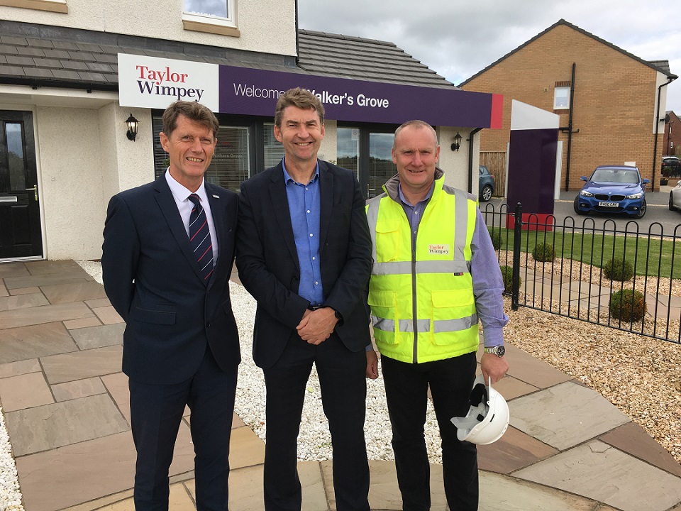 three men stood smiling at the camera outside of a taylor wimpey office