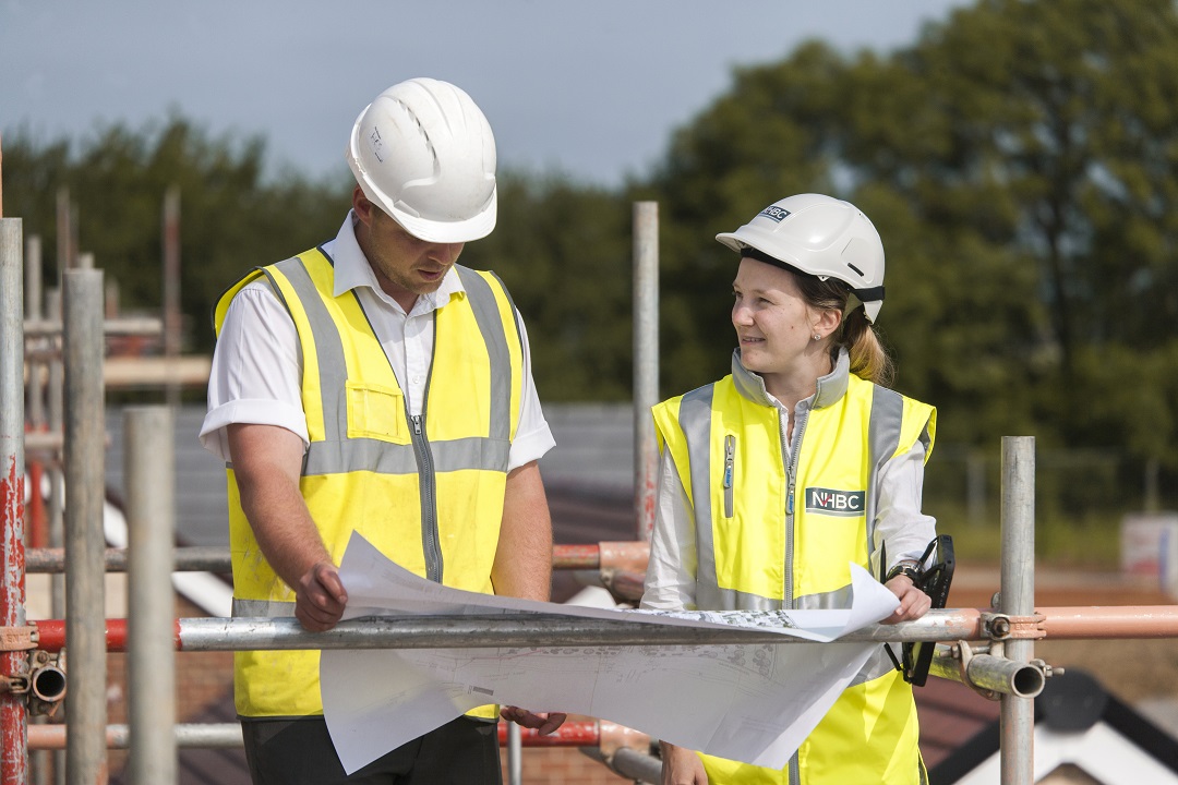 two people on site wearing site safety clothing and hard hats looking at plans