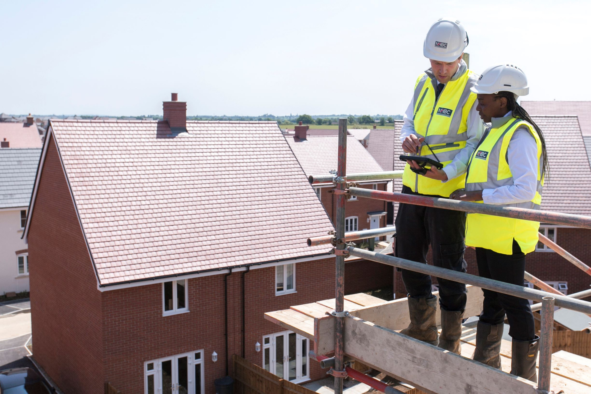 two people stood on scaffolding on site wearing site safety clothing looking at a tablet
