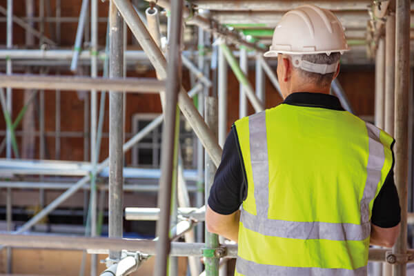 a person in site safety clothing and a hard hat walking through some scaffolding