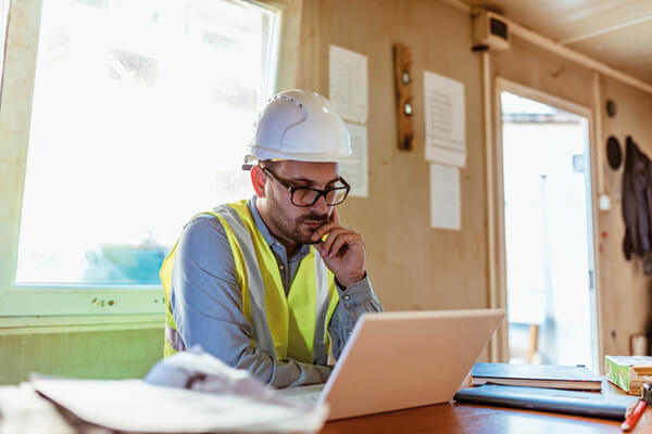 a man in site safety clothing and a hard hat looking at a laptop