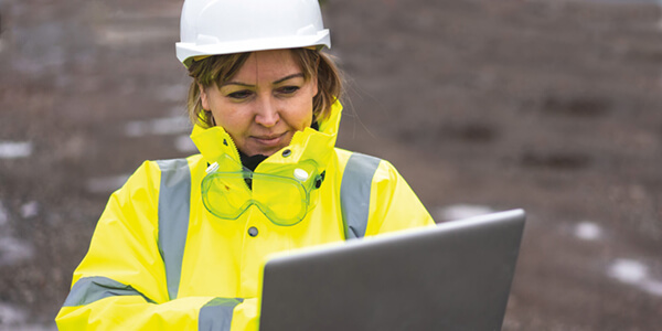 a woman in site safety clothing and a hard hat looking at a laptop