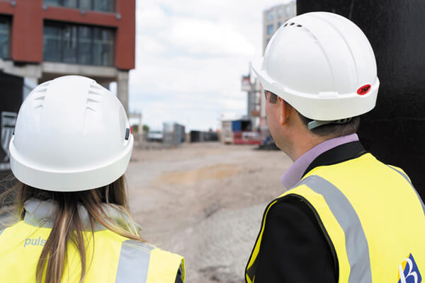 a man and a woman in site safety clothing and hard hat looking at a site