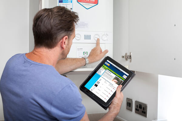 a man reading from a tablet while adjusting his boiler
