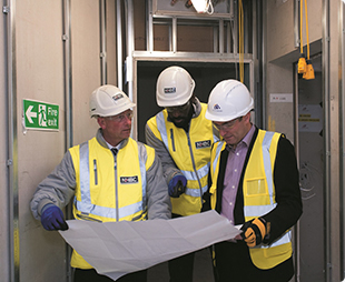three people wearing site safety clothing and hard hats inspecting plans