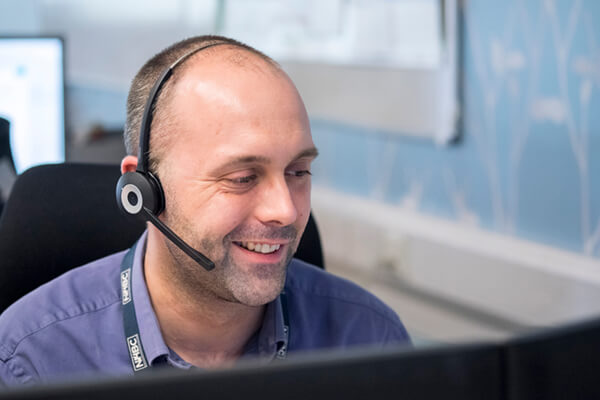 man sitting at his desk and smilinghile wearing a headset