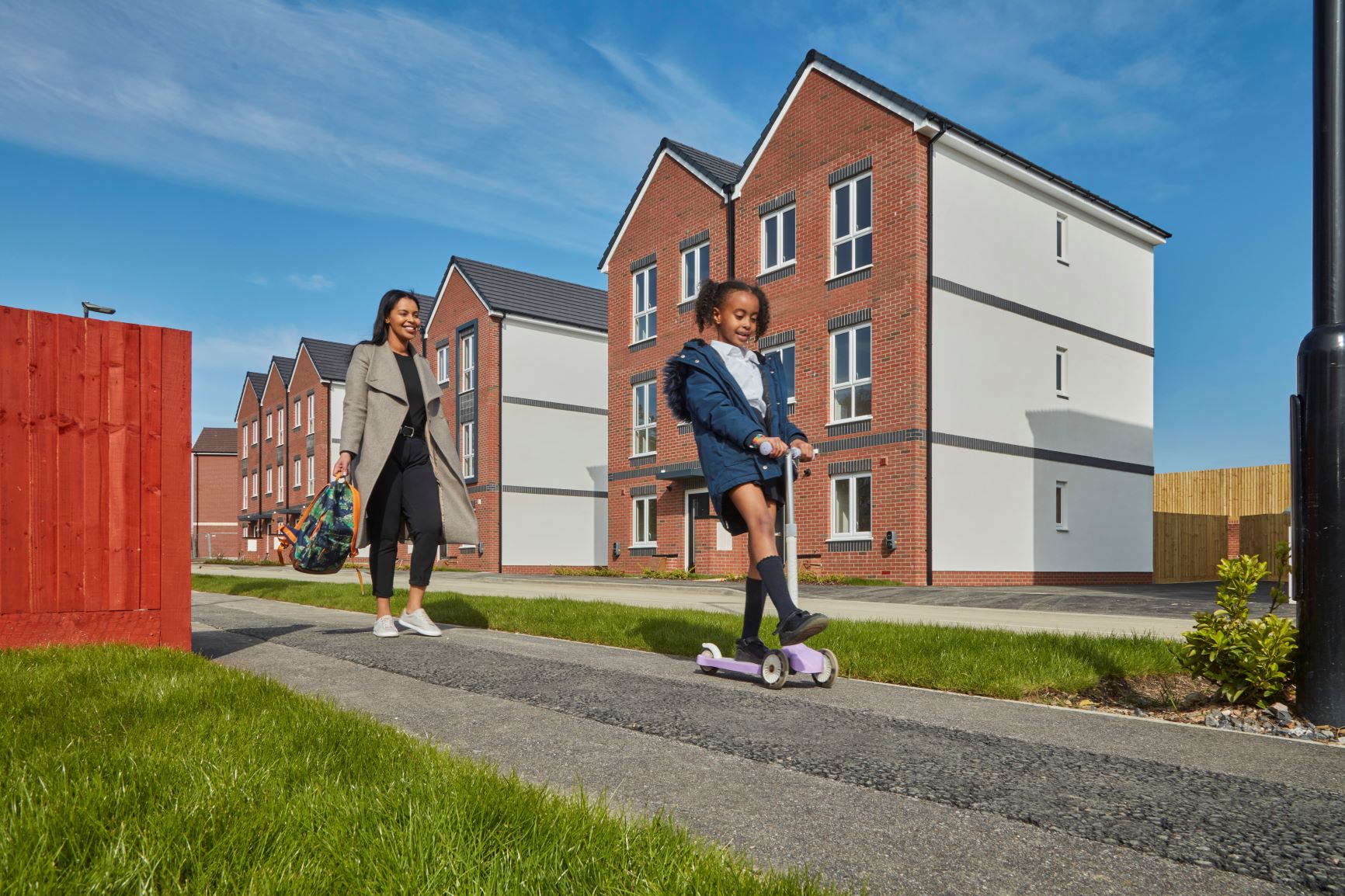 a girl on a scooter with her mum outside a new build property on a sunny day